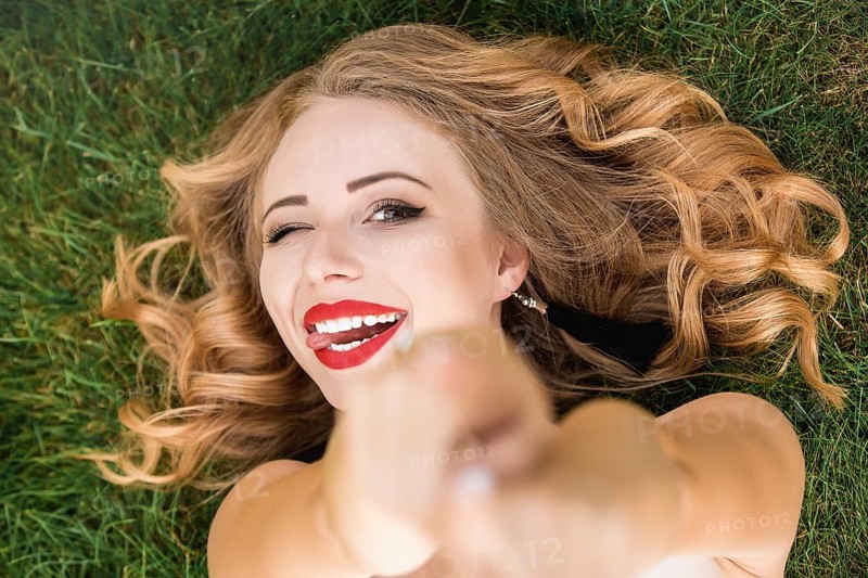 Caucasian pretty woman with curly black hair lying on the grass in the park. Smile and calm. portrait of Caucasian woman with blond hair spending day at nature.summer time