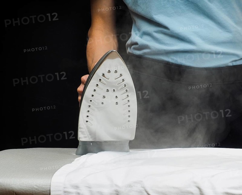 Male person using a steaming hot iron over a white shirt