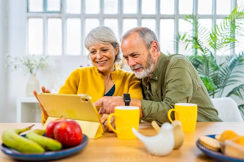 Happy caucasian modern senior couple surfing the net using digital tablet at home