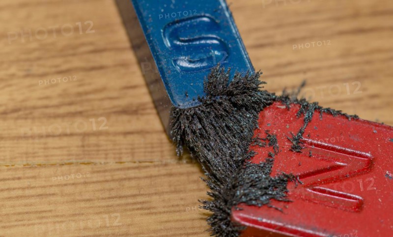 Closeup of iron filings attached to both the north and south end of colored magnets on wood grain background