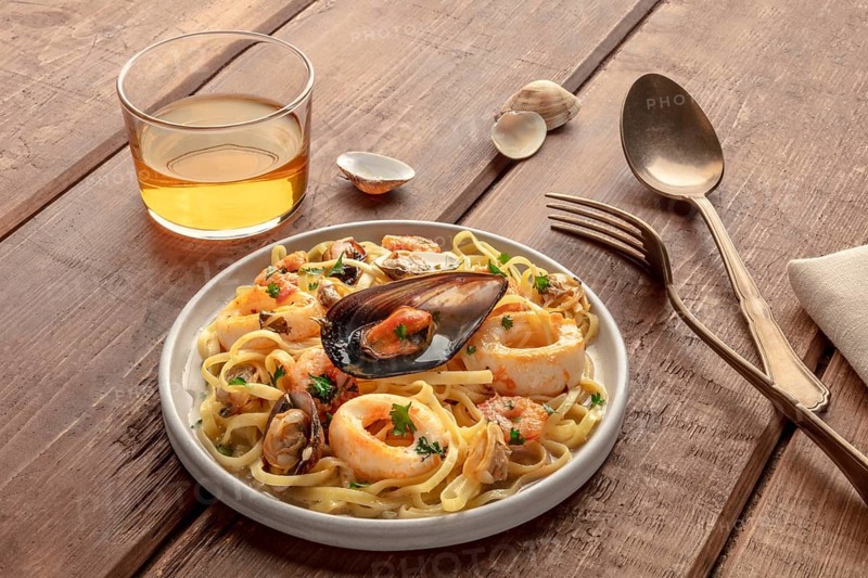 Seafood pasta. Tagliolini with mussels, shrimps, clams and squid rings, with a glass of wine on a dark rustic wooden background