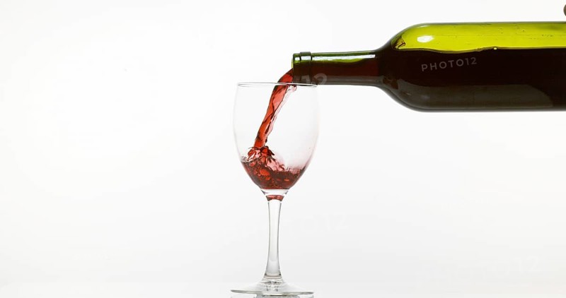 Red Wine being poured into Glass, against White Background