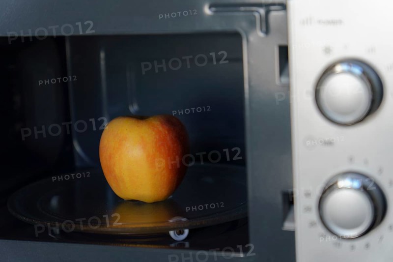 A fresh red apple placed inside a microwave oven