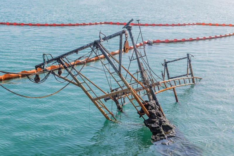 Rusty remnants of a sunken ship with booms and an orange barrier on calm ocean water, in Sinjin-do, South Korea, Asia