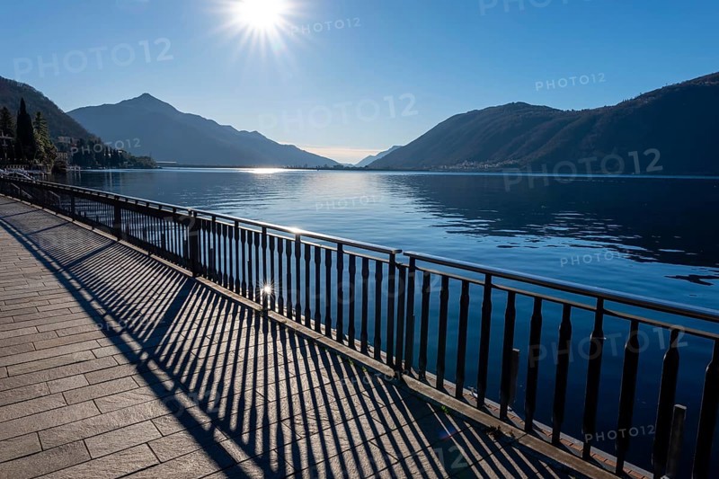 Shadow of a Railing on the Street on the Waterfront to Lake Ceresio with Mountain and Sunbeam in Campione d'Italia, Lombardy, Italy, Europe