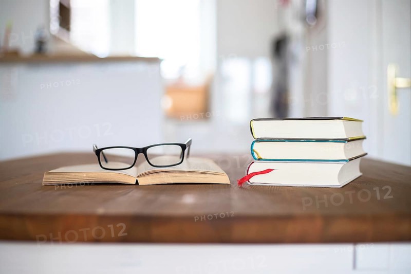 Stack of books and glasses lying on wooden desk at home. Knowledge and science