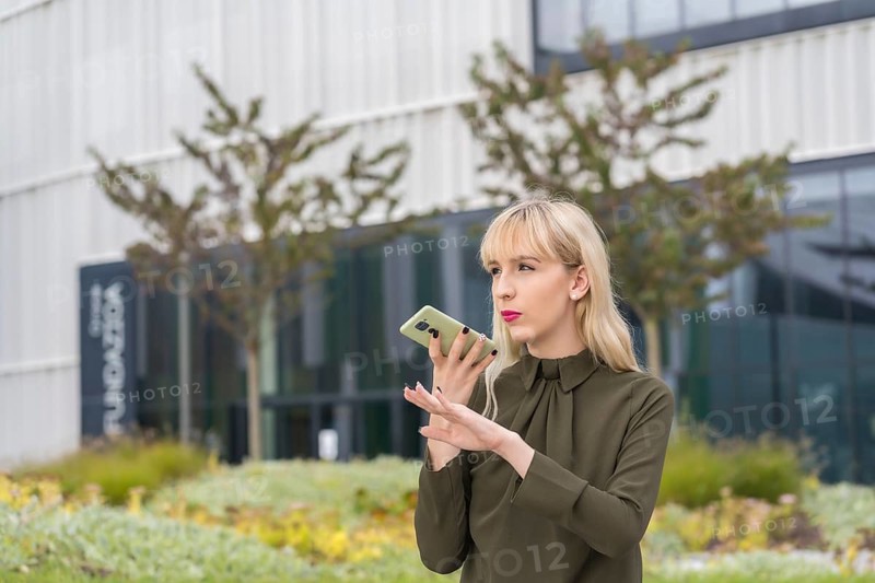 Caucasian blonde entrepreneur girl in a business park sending an audio note with the phone