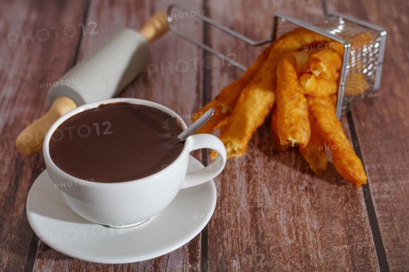 White cup of hot chocolate with churros typical spanish breakfast on a wooden table