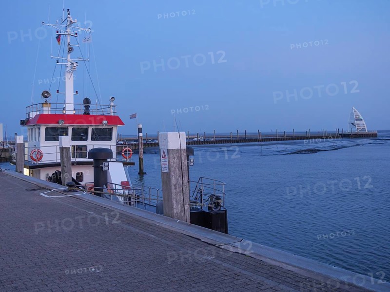 A ship lies at the dock of a harbour at dusk, the calm waters reflect the evening light, juist, east frisia, germany