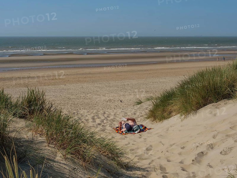 Person relaxing on a blanket in a sand dune on the beach, overlooking the calm sea, de haan, belgium