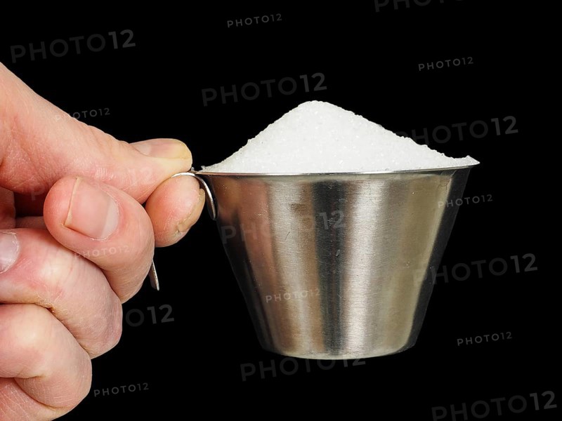 Person holding a measuring cup of one deciliter filled up with white granulated sugar, isolated on black