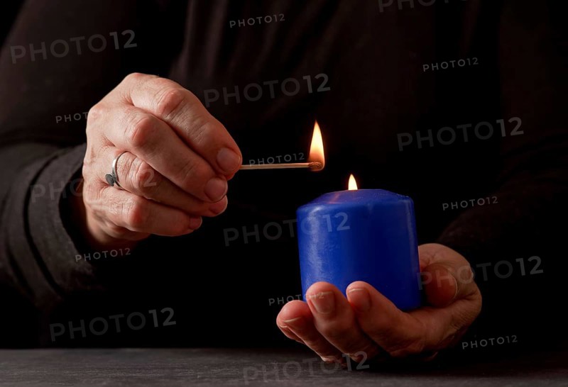 Hands of a woman lighting a blue candle with a match