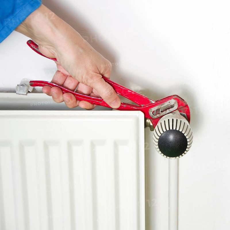 Plumber fixing a radiator with red pliers