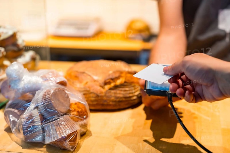 Customer in the bakery shop buying an artisan bread from the baker in the workshop, paying with the card