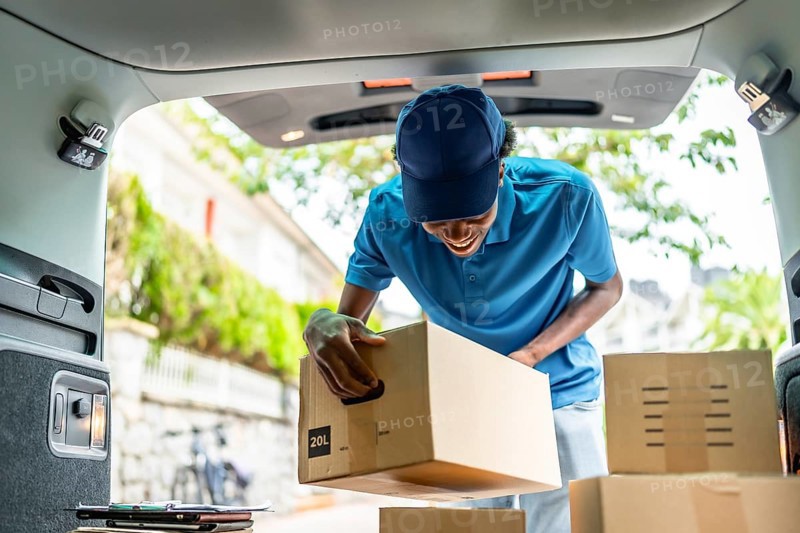 Delivery african man with blue uniform and cap working with several packages on van