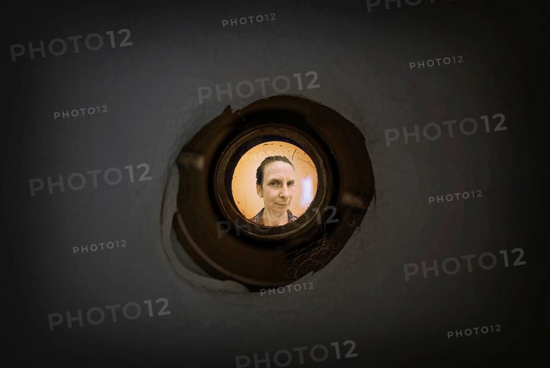 Woman seen out of focus through the old dirty peephole of the front door of a dark apartment