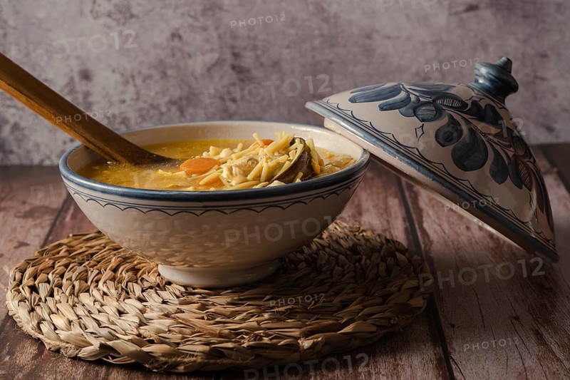 Tureen decorated with chicken soup with noodles on a wooden table