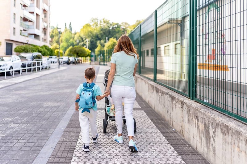 Rear view of a mother and son going to school together holding hands on the first day of school