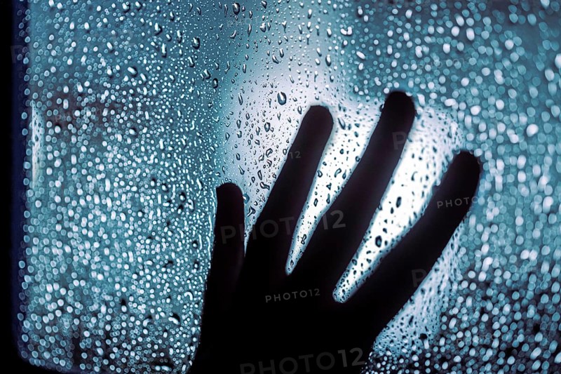 Close up of hand silhouette on window with water drops, night