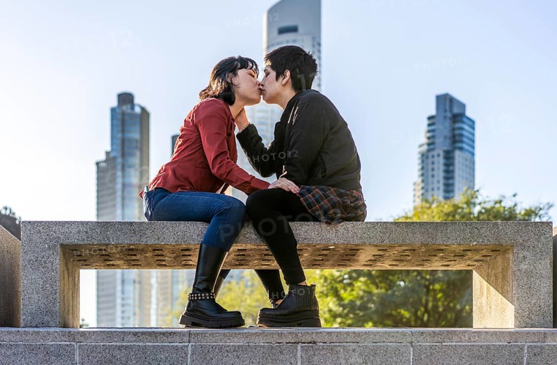 Charming low-angle view of a young couple of women sharing a loving kiss on a bench in the park