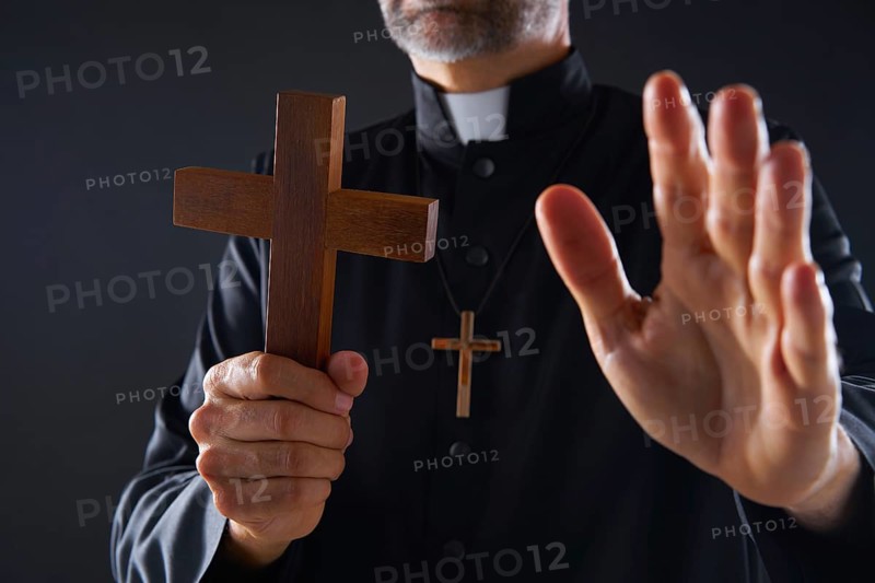 Priest holding cross of wood praying in foreground