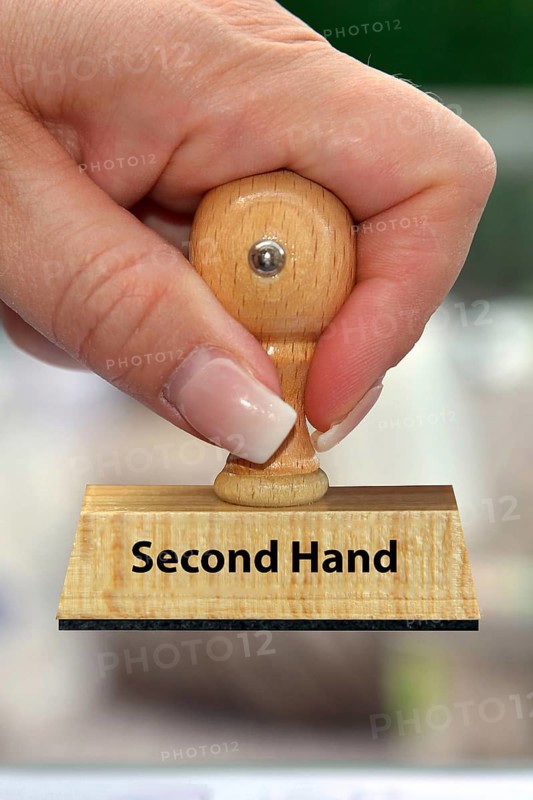 A woman's hand holds a wooden stamp with the inscription: Second Hand