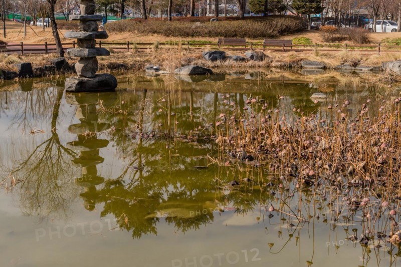 Stone tower in small pond in city park on sunny winter day in South Korea