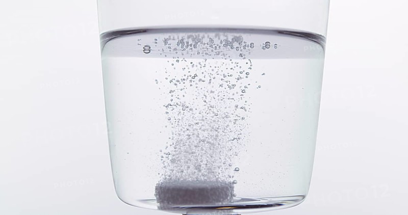 Tablets Falling and Dissolving into a Glass of Water against White Background