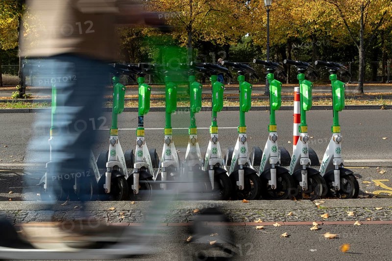 Traffic, mobility, motion blur, scooter riders and lined-up e-scooters from the provider Lime in autumn on a street in Berlin, Germany, Europe