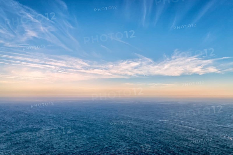Beautiful seascape with calm sea or ocean waves. Atmospheric haze, colorful low clouds lit by sundown at horizon, high romantic clouds in clear blue sky. Beauty in nature, idyllic landscape, perfect background, natural backdrop