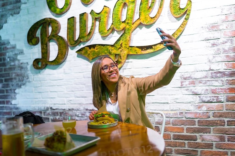 Happy latin blonde woman taking selfie while eating a tasty hamburger at fast food restaurant