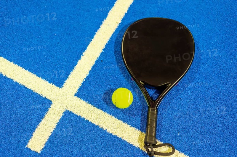 Top view of a single paddle tennis racket and ball in a blue court