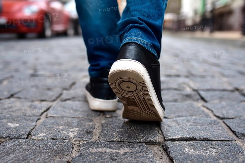 Legs view of a male walking on the road in the city. close up of black male shoes