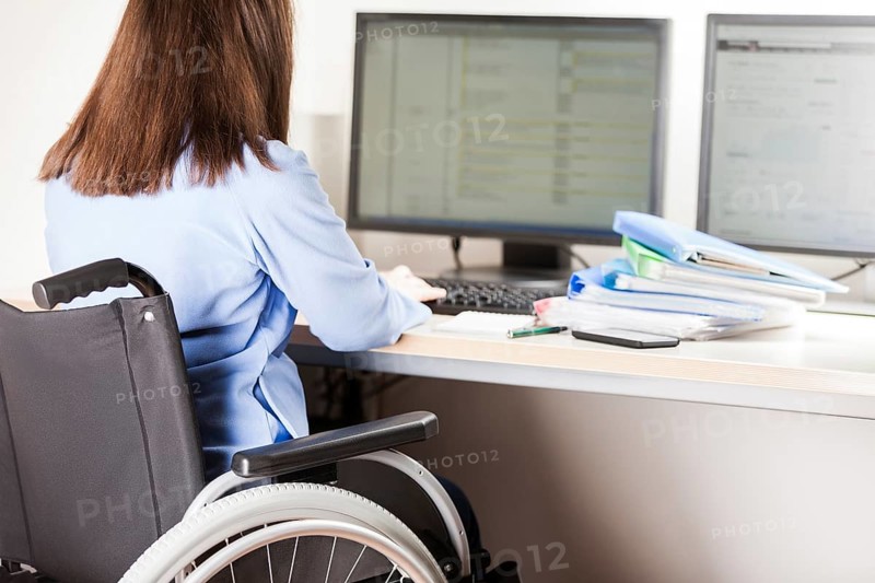 Invalid or disabled young business woman person sitting wheelchair working office desk computer