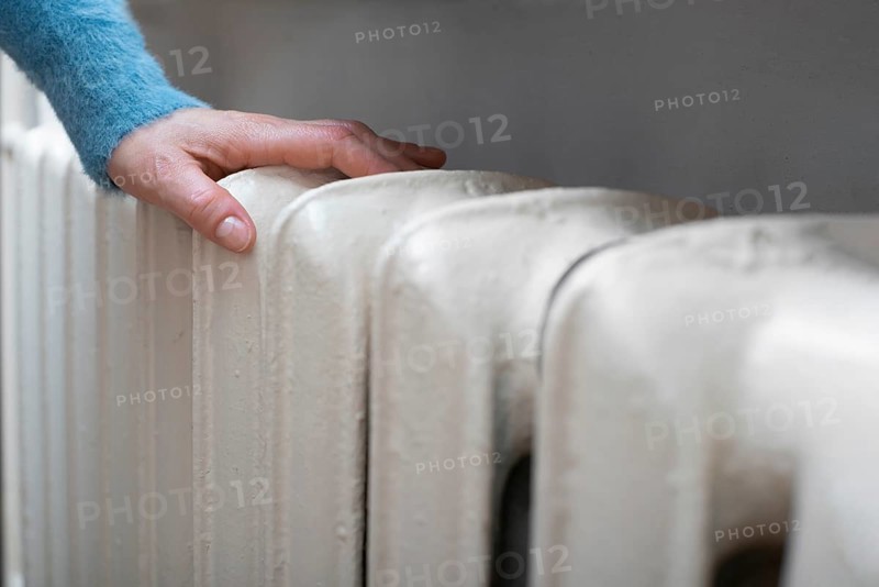 Caucasian female warming up hands near Hot Water Radiator. Space for text
