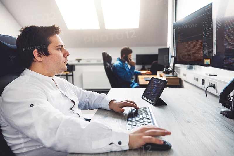 IT Programmer Working on Desktop Computer. Male Specialist Creating Innovative Software Engineer Developing App, Program, Video Game. Terminal with Coding Language. Over Shoulder.
