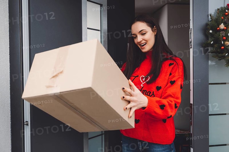 Cheerful young woman excited over a package she just received. Woman getting her christmas gift in the mail. Opening the Christmas present at home