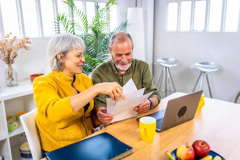 Senior couple working together on their home budget using laptop and holding papers