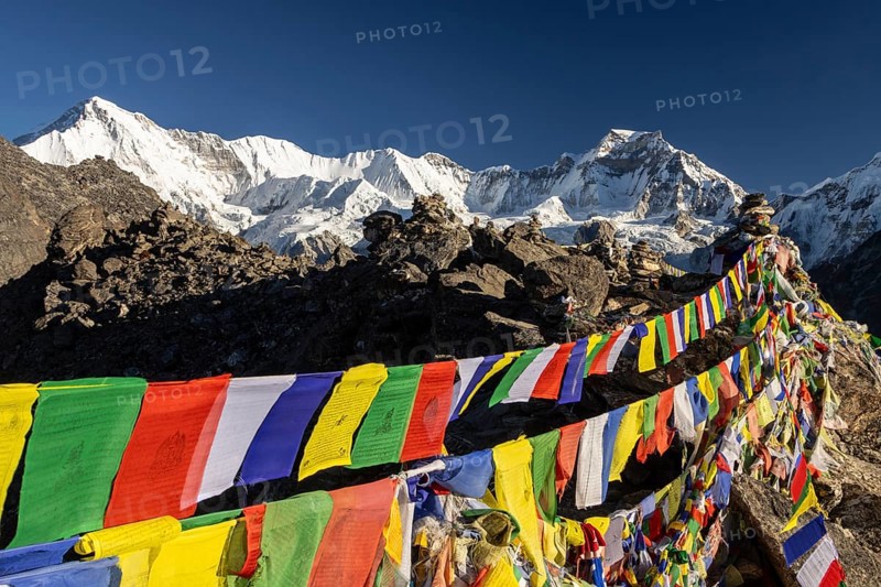 Buddhist prayer flags marking the summit of Gokyo Ri, the popular trekking peak in the Everest Region, seen just after the sunrise on a sunny, November day. The eight-thousander Cho Oyu, the sixth-highest mountain on the planet, is on the left-hand side in the background. Right of it, on the same ridge, there are: Tenzing Peak, Ngozumpa Kang, Hillary Peak and Gyachung Kang, which is the highest seven-thousander in the world. Khumbu Region, Himalayas. Sagarmatha National Park, the UNESCO World Heritage Site.