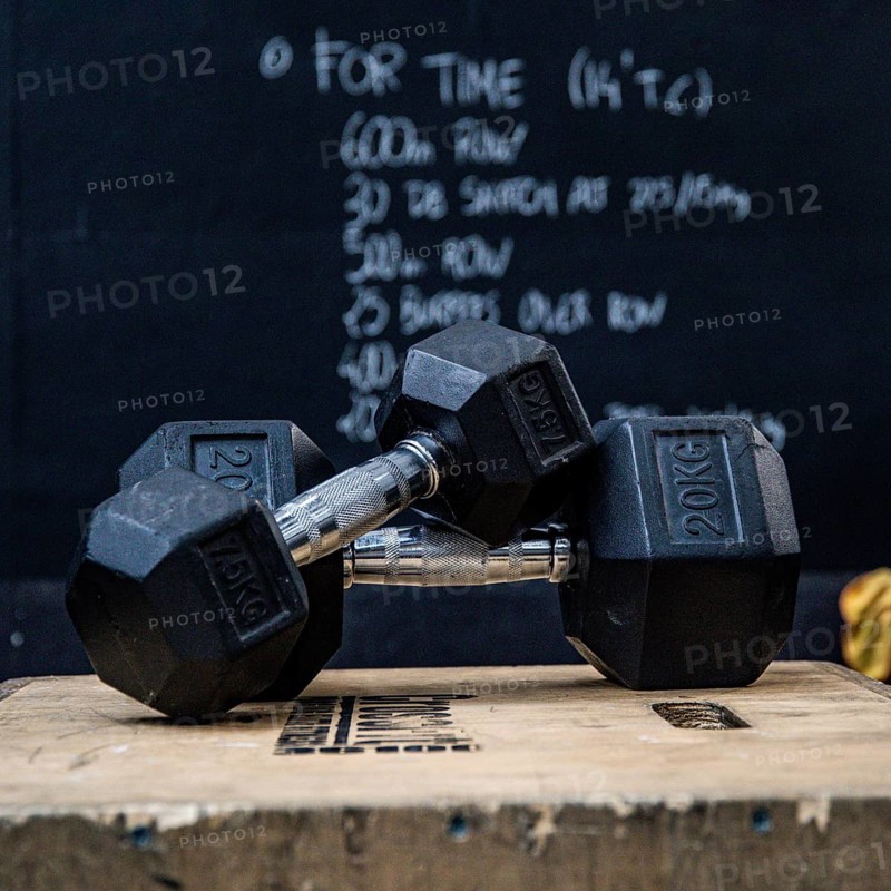 Closeup of two dumbbells on a wooden box in front of blackboard at the gym. Wod, workout of the day
