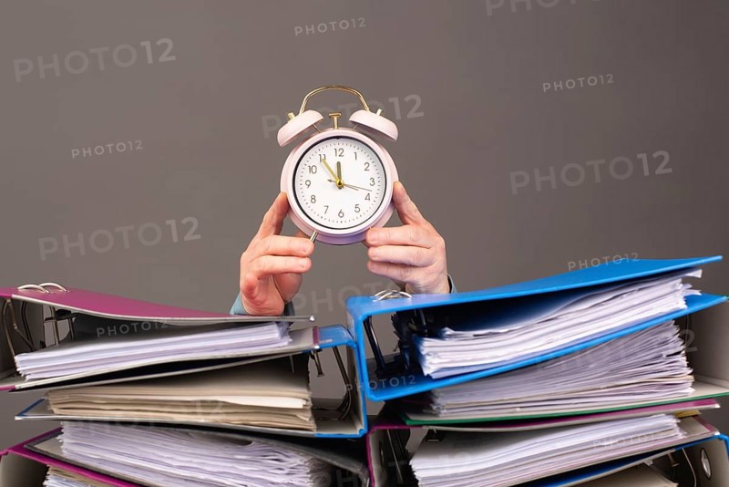 Alarm clock standing next to pile of file folders, burnout, stress and overworked, pressure at work, deadline
