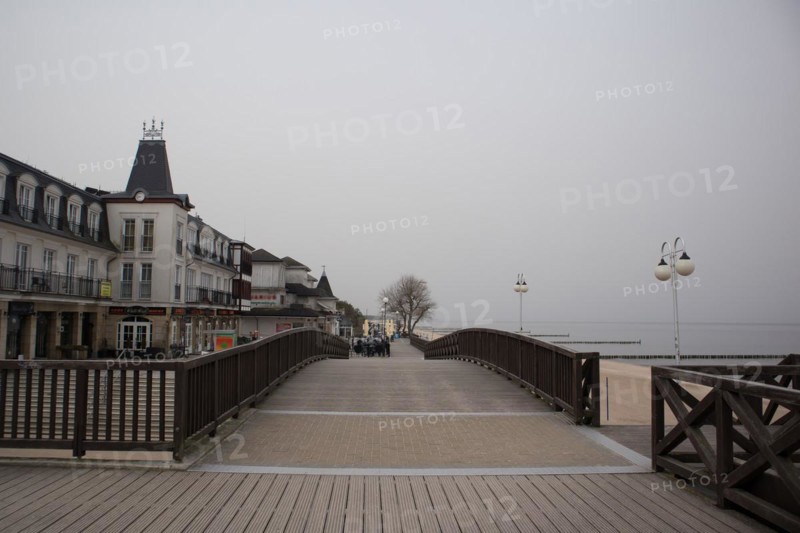 Overcast day on a boardwalk with people walking near waterfront buildings and street lamps, Mielno, Poland, Europe