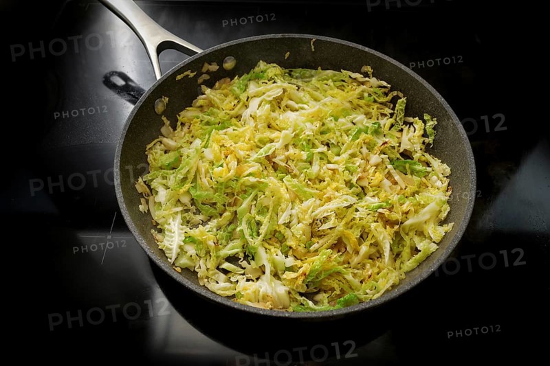Savoy cabbage in a frying pan on the black stove, cooking at home with healthy winter vegetables, selected focus, narrow depth of field
