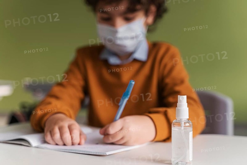 Front view child with medical mask class with bottle hand sanitizer desk