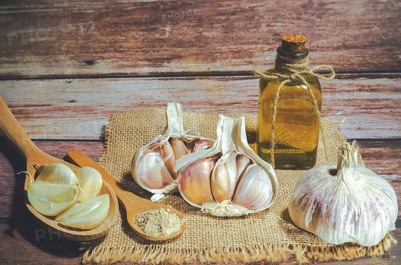 Whole, powdered and chopped garlic on a burlap cloth with a glass bottle with olive oil on a wooden table