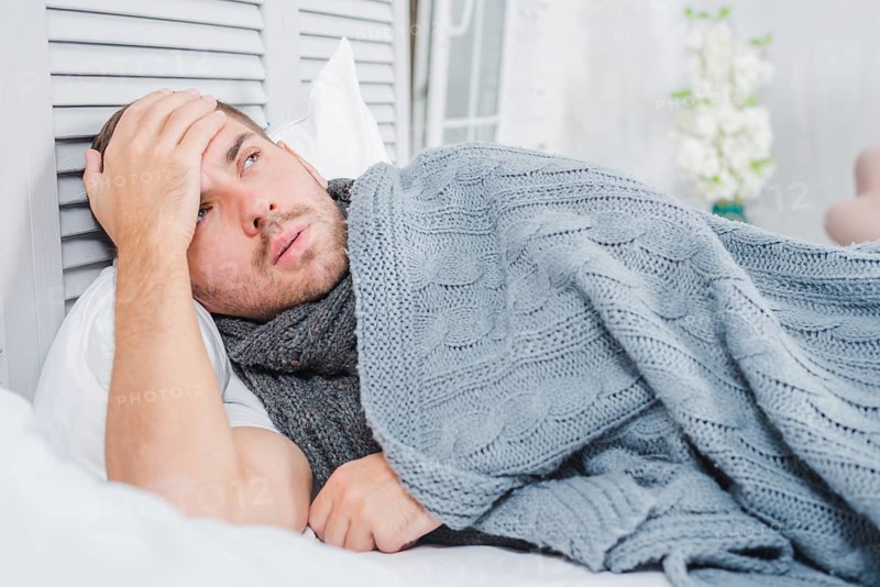 Young man lying bed with headache fever touching his forehead