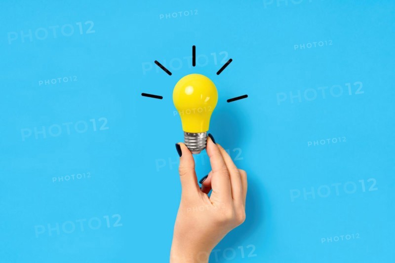 Female hand hold yellow light bulb on blue background. Creative idea, innovation, brainstorming concept