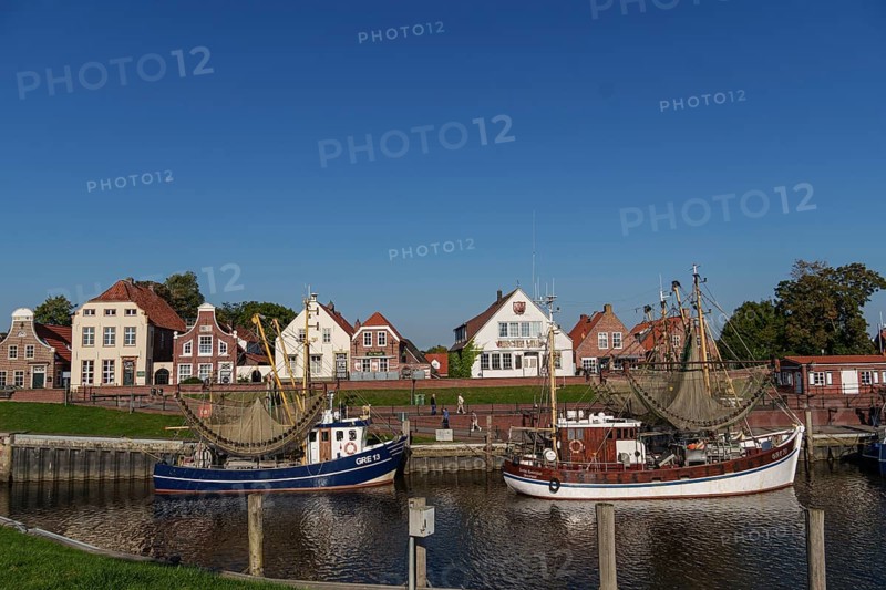 A quiet harbour with two boats and picturesque brick houses under a clear blue sky, Greetsiel, East Frisia, Germany, Europe