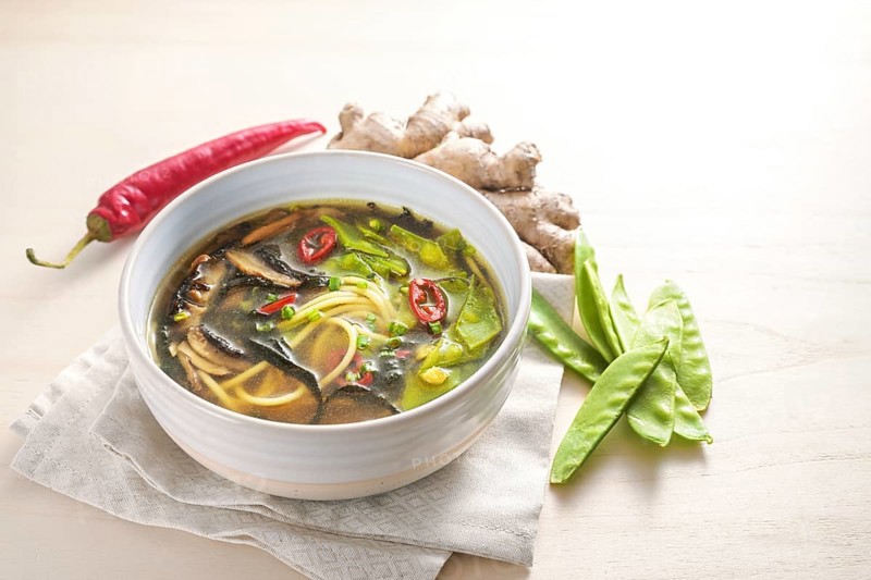 Spicy Asian vegetable soup with noodles, miso, nori seaweed, ginger and chili in a bowl on a wooden table, copy space, selected focus, narrow depth of field