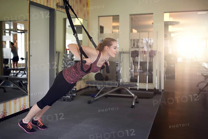 Young fit blond woman exercising with suspension bands in a modern gym in the morning
